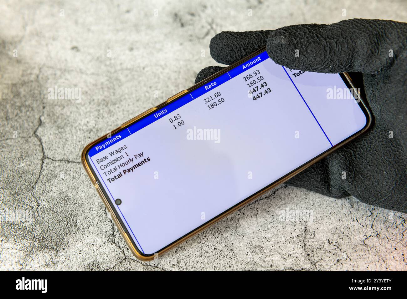 Un lavoratore che indossa guanti da lavoro con uno smartphone e una busta paga digitale dei guadagni salariali. Foto Stock