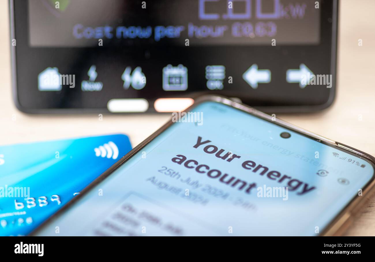 Un concetto di costo energetico con bolletta digitale su uno smartphone, una carta bancaria e un contatore di energia intelligente. Foto Stock