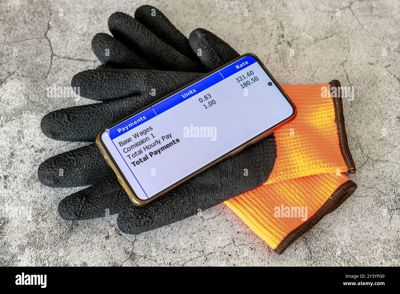 Un concetto di salario di lavoro con uno smartphone con una busta paga digitale sopra un paio di guanti da lavoro isolati in uno sfondo di cemento. Foto Stock