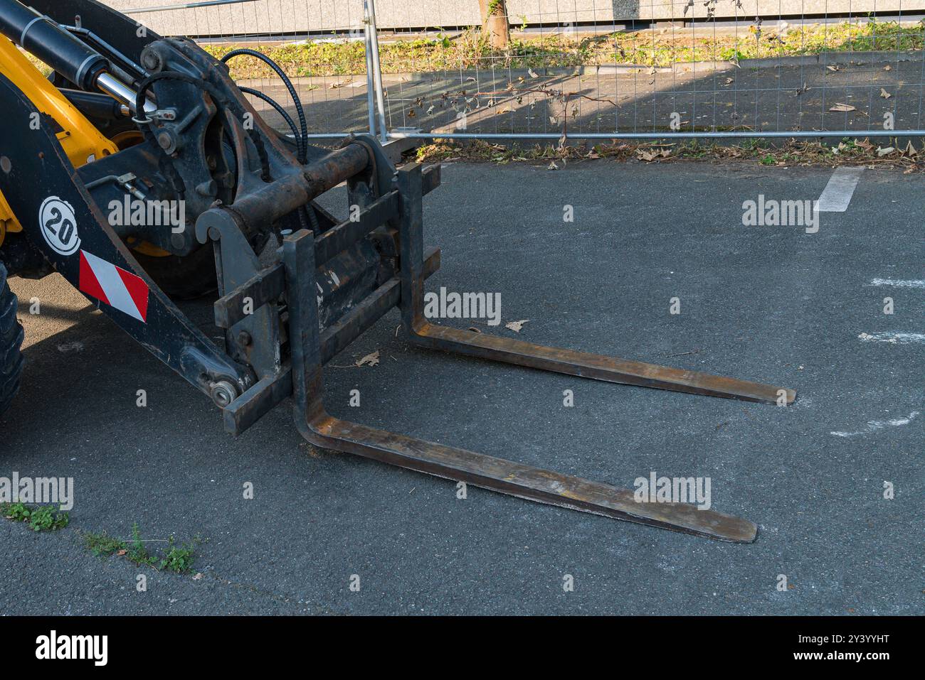 Un carrello elevatore a forche rimane inattivo in un cantiere edile, mostrando le forche estese. L'area è contrassegnata da una recinzione temporanea, con una superficie asfaltata pulita e. Foto Stock