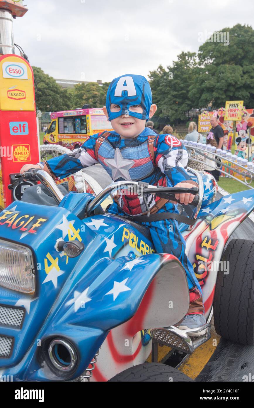 Little 'Captain America', supereroe dei fumetti Marvel che si gode un giro al Saltaire Festival 2024 che si tiene a Roberts Park il 14 settembre 2024 Foto Stock