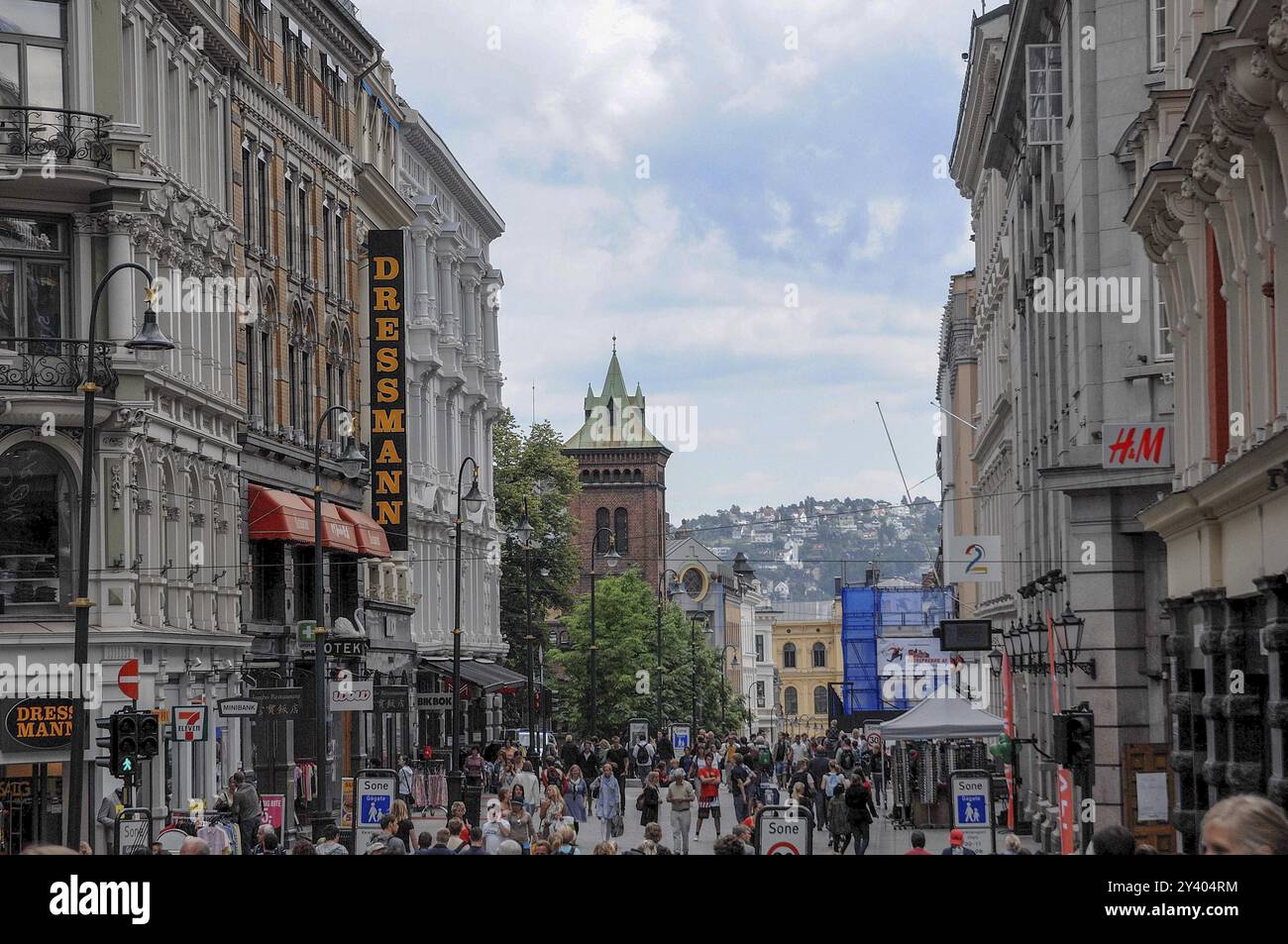 Strada trafficata per lo shopping con diversi negozi, sullo sfondo un panorama collinare e un cielo nuvoloso, oslo, norvegia Foto Stock