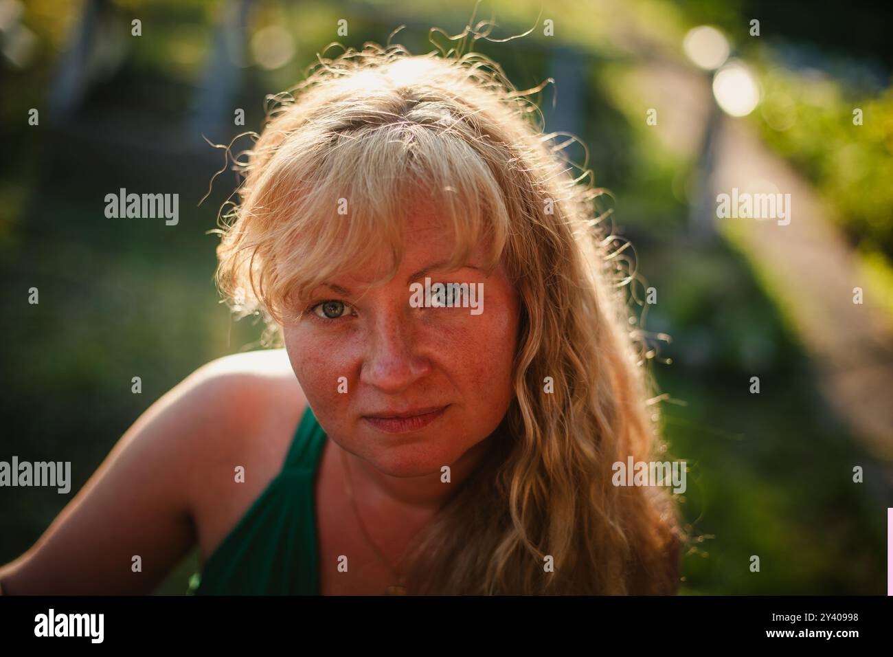 Un ritratto ravvicinato di una donna con i capelli di colore paglia, in piedi in un campo illuminato dal sole, il suo viso è delicatamente illuminato dalla luce calda del sole. Foto Stock