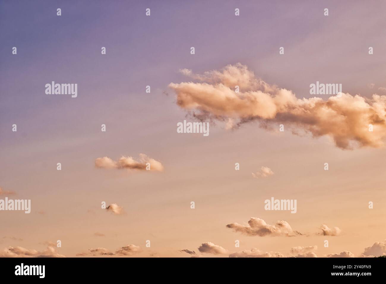 Un cielo sereno al tramonto con morbide e soffici nuvole sparse su uno sfondo sfumato di colori caldi. Foto Stock