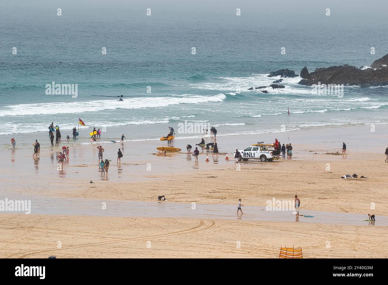 Una vivace spiaggia con gente che si diverte a varie attività. Sono presenti bagnini e alcuni individui stanno navigando in acqua. La spiaggia è sabbiosa Foto Stock