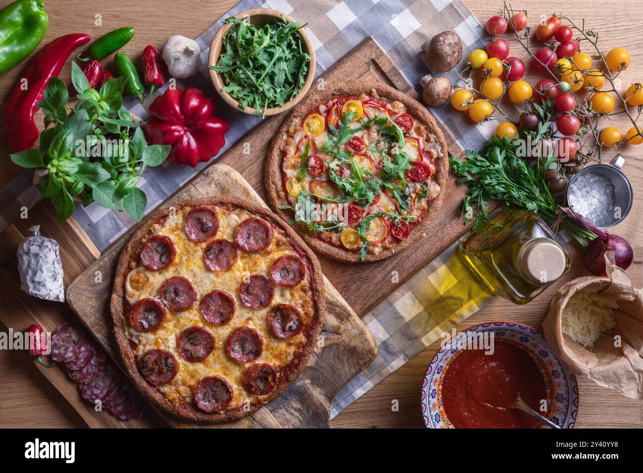 Preparare la pizza con salame, formaggio, salsa, pomodori, verdure ed erbe fresche su fondo di legno. Vista dall'alto Foto Stock