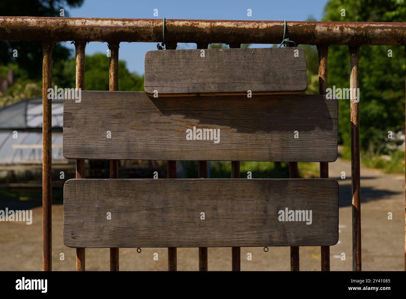 Tre tavole rustiche di legno, vuote e in attesa di messaggi, si aggirano da un cancello intempestivo circondato da una vibrante vegetazione sotto un cielo blu luminoso, invitante Foto Stock