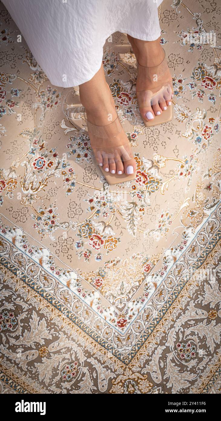 Una donna con un abbigliamento tradizionale bianco seduto su una scala di tappeti persiani dal design complesso, tenendo in mano una tazza di caffè. Foto Stock