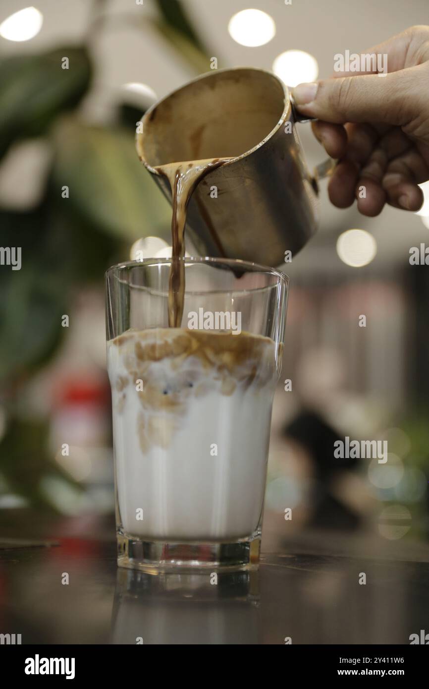 L'espresso appena estratto viene versato su latte freddo e ghiaccio, creando una bella bevanda a strati. Foto Stock