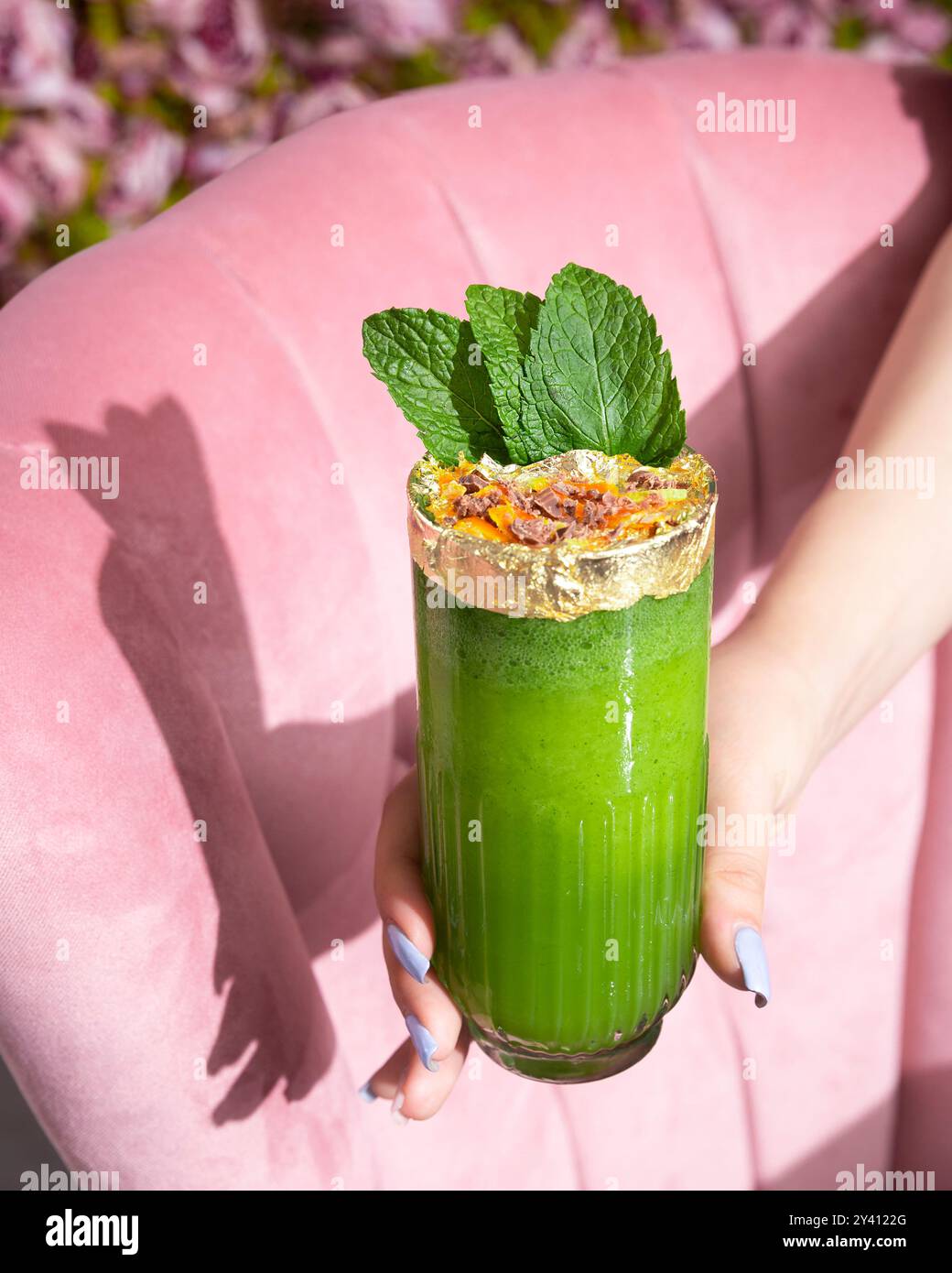 Una vivace bevanda verde guarnita con menta fresca e fiocchi dorati, tenuta in un elegante bicchiere. Foto Stock