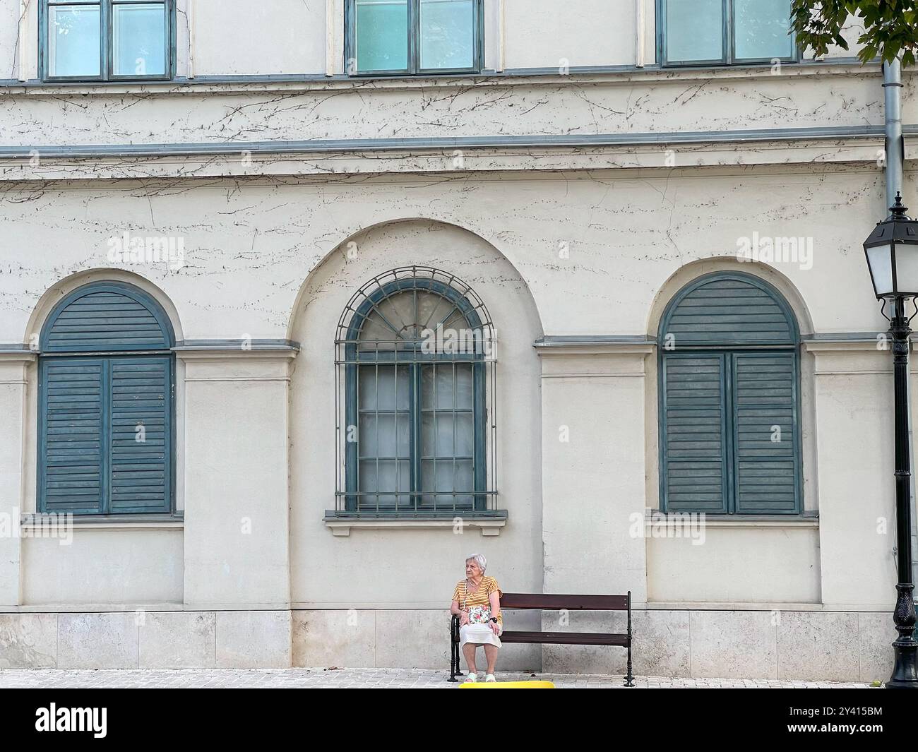 Budapest, Ungheria - 8 settembre 2024: Donna anziana solitaria seduta sulla panchina vicino all'edificio Foto Stock