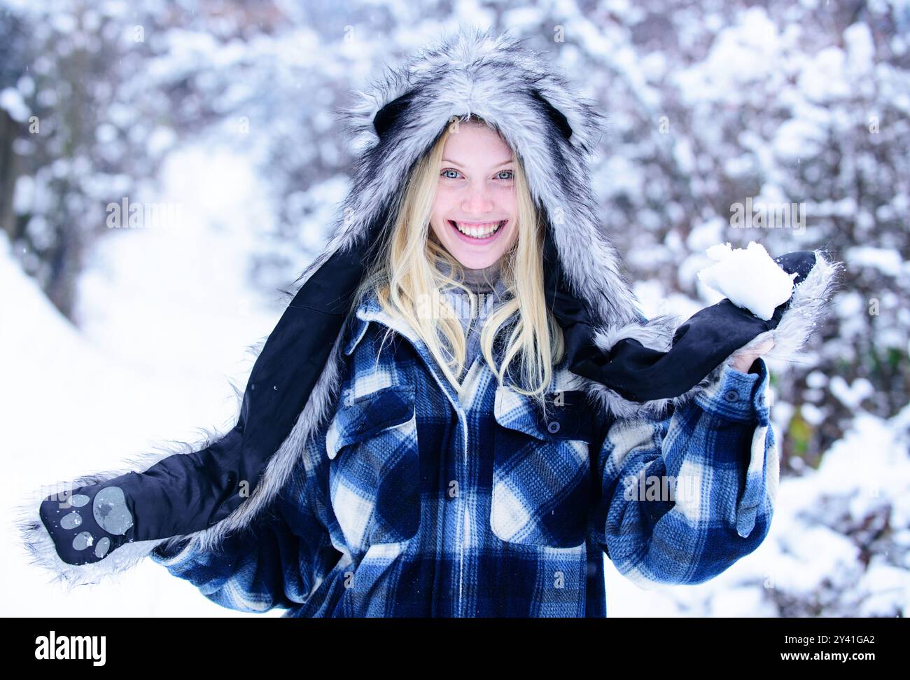 Inverno. Donna sorridente che gioca con la neve nel parco invernale. Ragazza giocosa in abiti caldi con palla di neve. Attività per le vacanze invernali. Felice ragazza che ha f Foto Stock