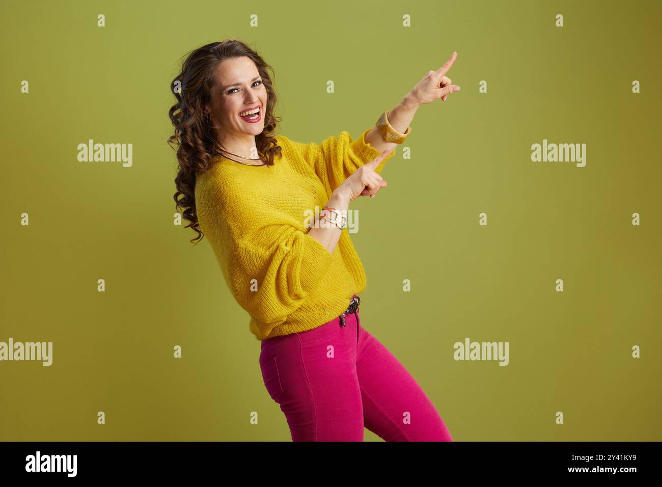 donna moderna sorridente isolata sul verde in maglione giallo. Foto Stock