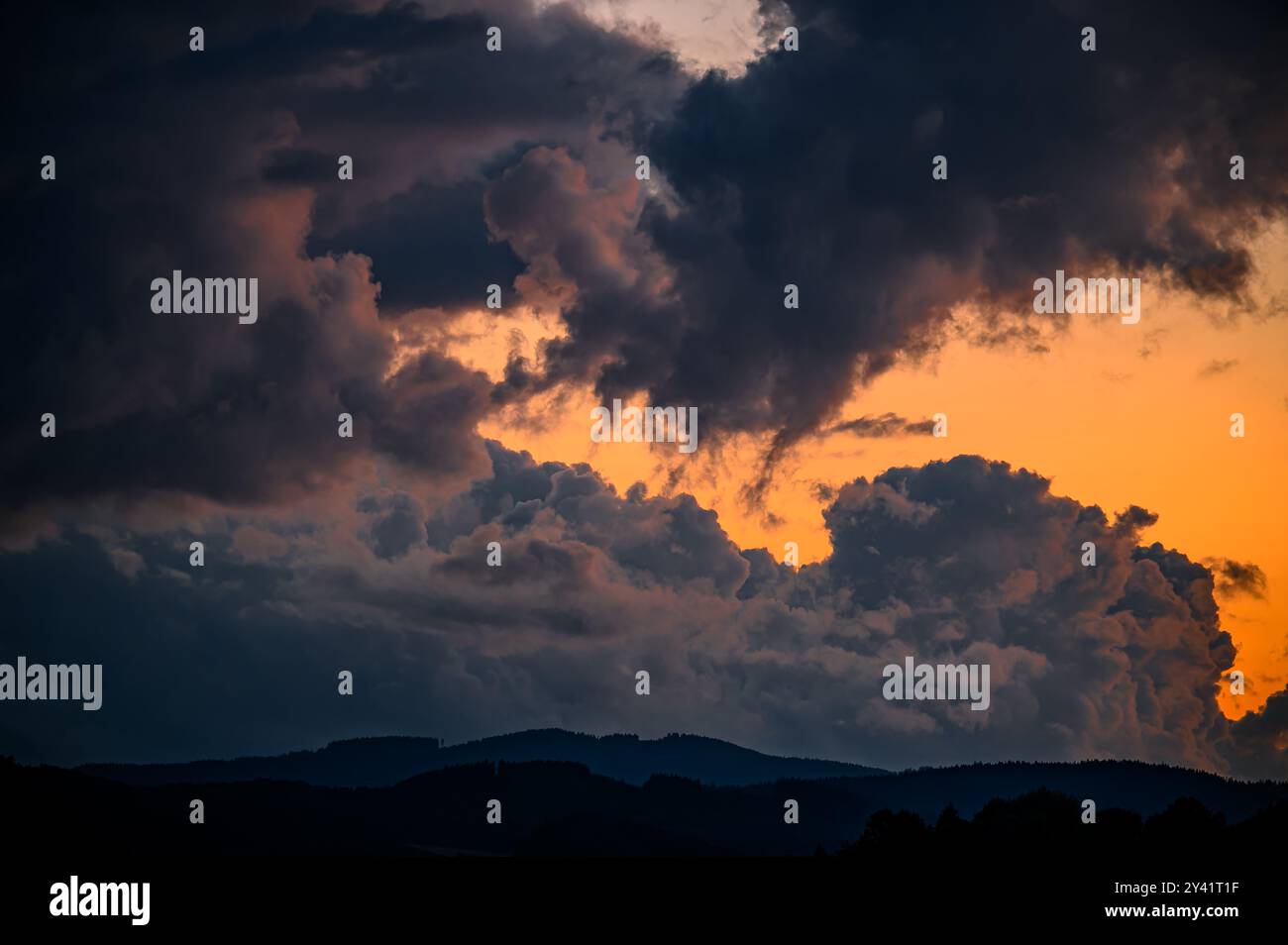 Una vista spettacolare del cielo dopo il tramonto con un bagliore arancione e nuvole dall'aspetto inquietante. La parte inferiore della scenografia presenta fitte foreste. Foto Stock