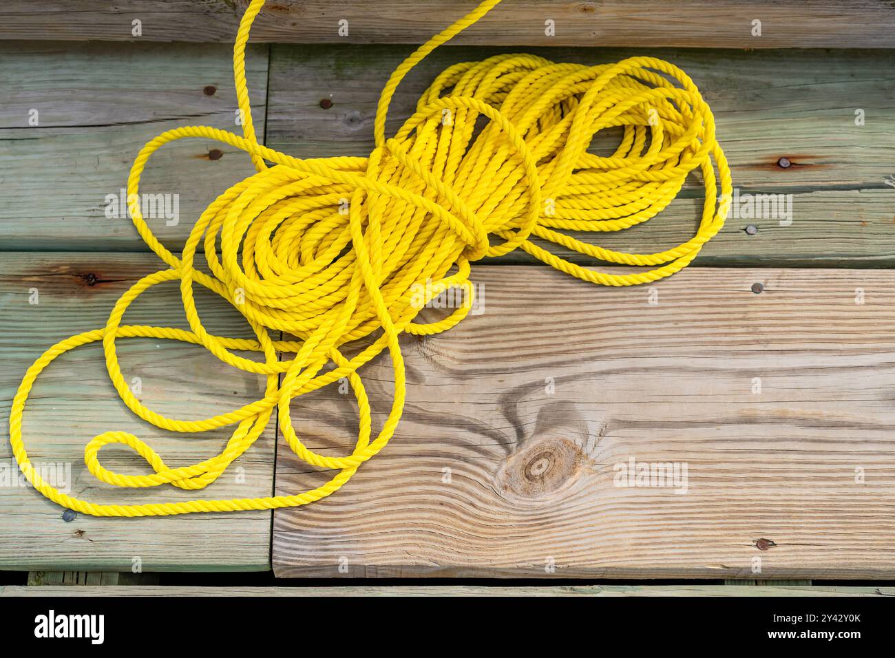 Fune gialla in nylon, collegata a un anello di salvataggio arancione, seduta su un molo di legno. Foto Stock