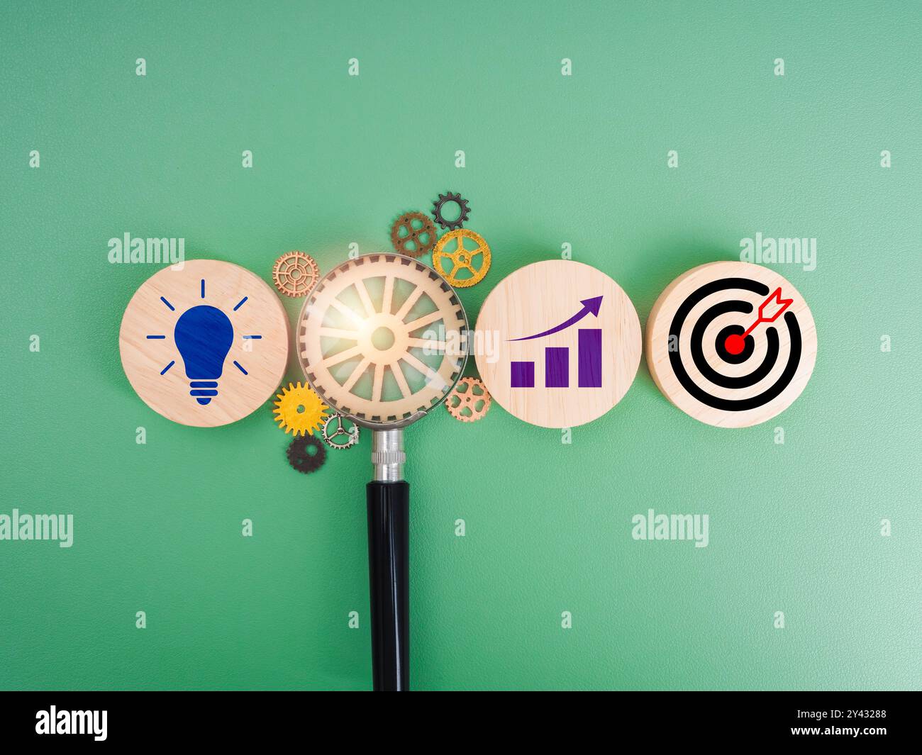 Icona target, simbolo della lampadina creativa e simbolo del grafico di crescita su blocchi di legno con ingranaggio in lente di ingrandimento su sfondo verde. Strato aziendale Foto Stock