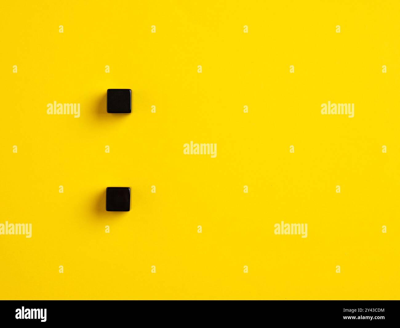 Il segno di punteggiatura del simbolo dei due punti. Due cubi neri su sfondo giallo. Foto Stock