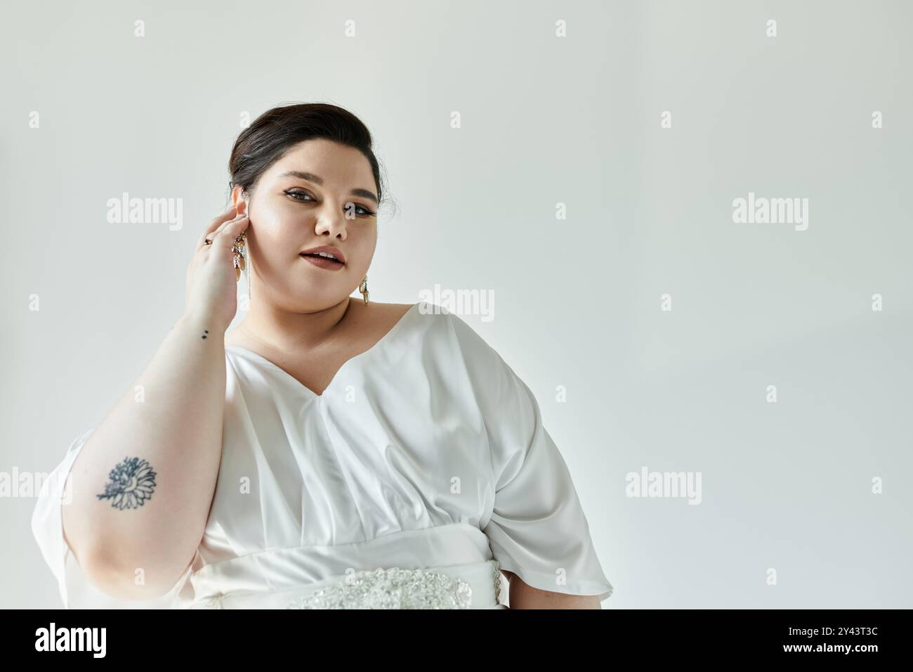 Una splendida sposa di grandi dimensioni presenta il suo abito da sposa e gli orecchini, irradiando eleganza e grazia. Foto Stock