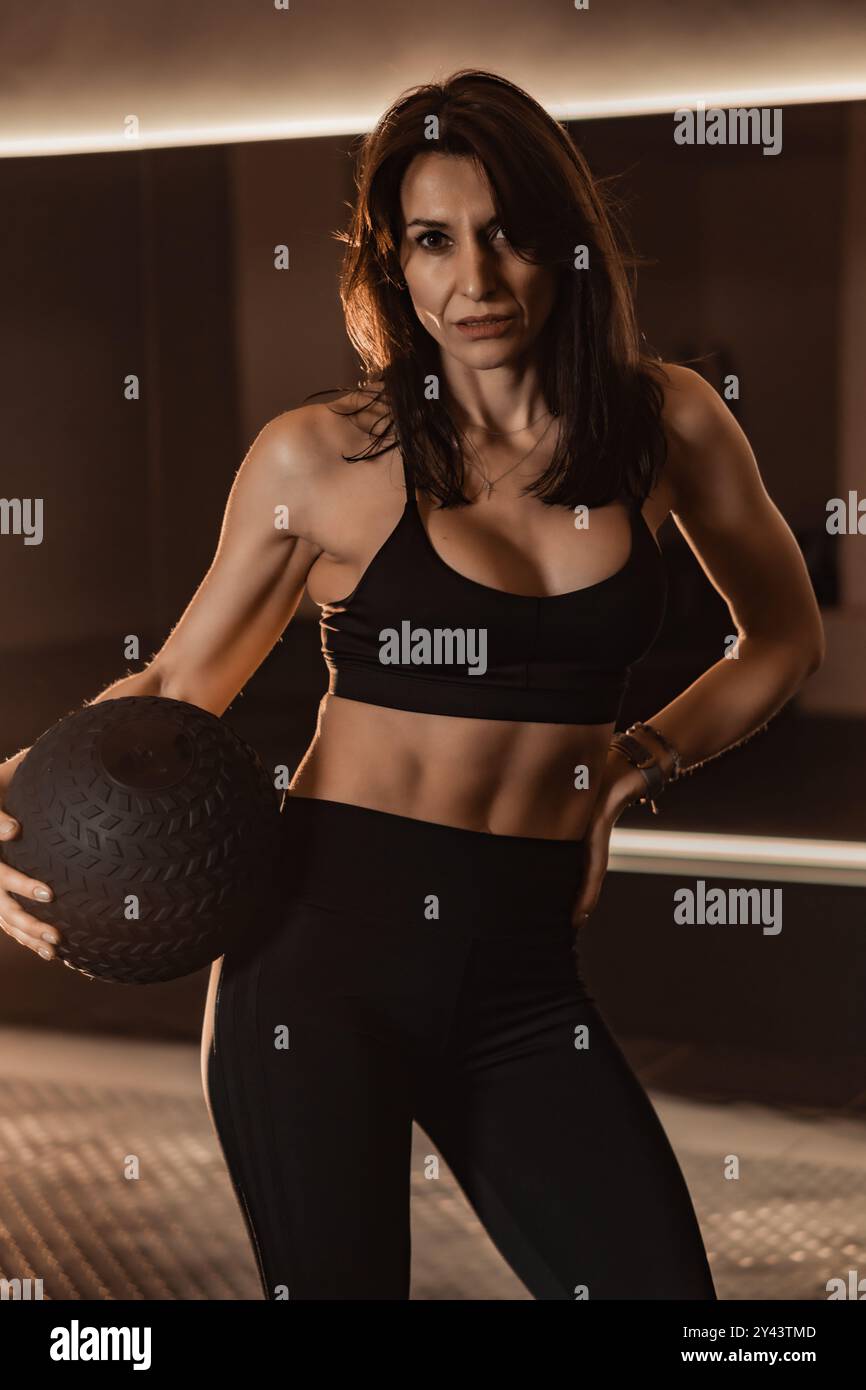 Unisciti a noi per una sessione di fitness dinamica con una donna che mostra le sue abilità con una palla medica in un ambiente elegante e moderno, perfetto per Foto Stock