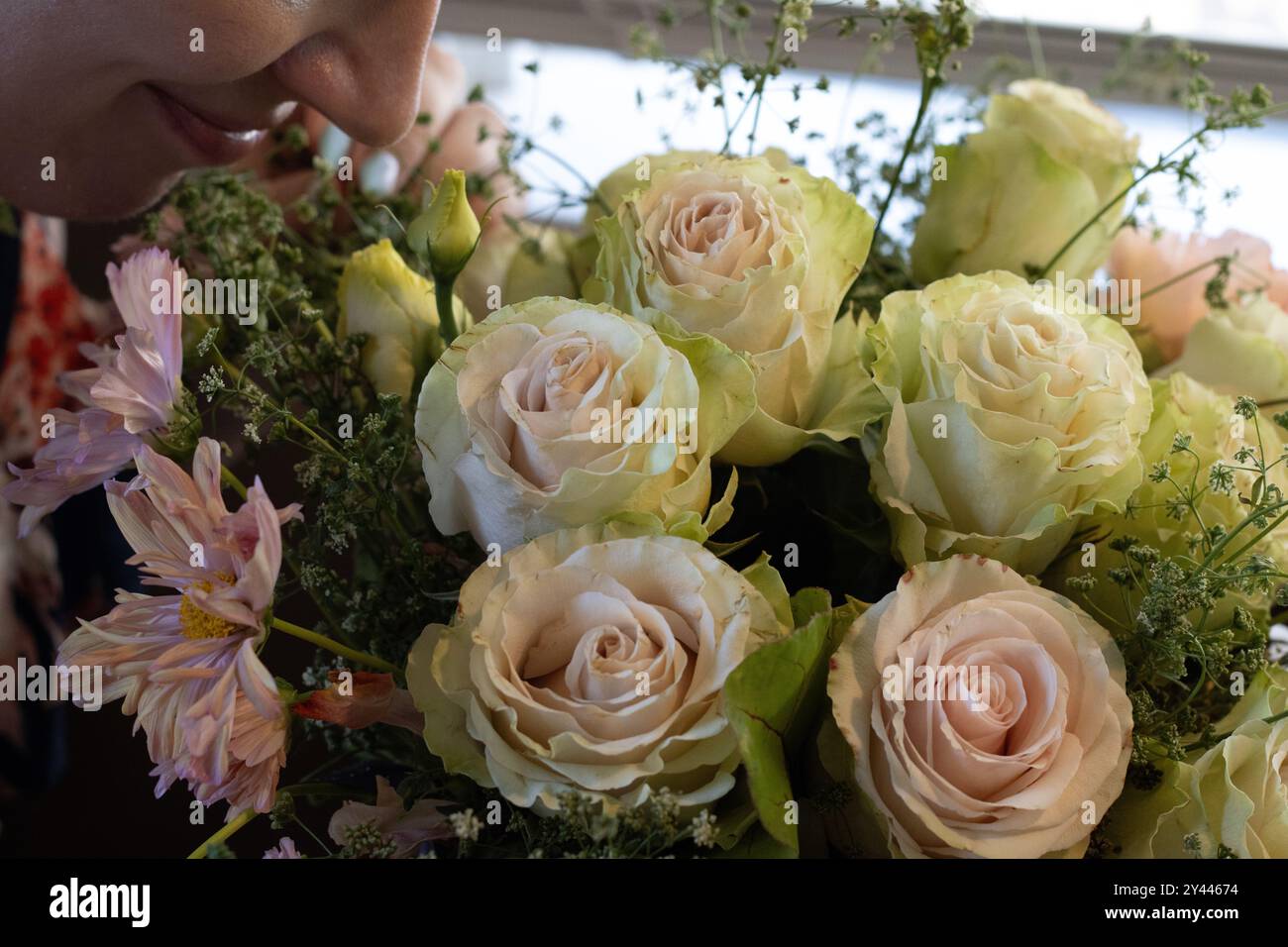 Donna che profuma un fresco bouquet di rose e fiori misti Foto Stock