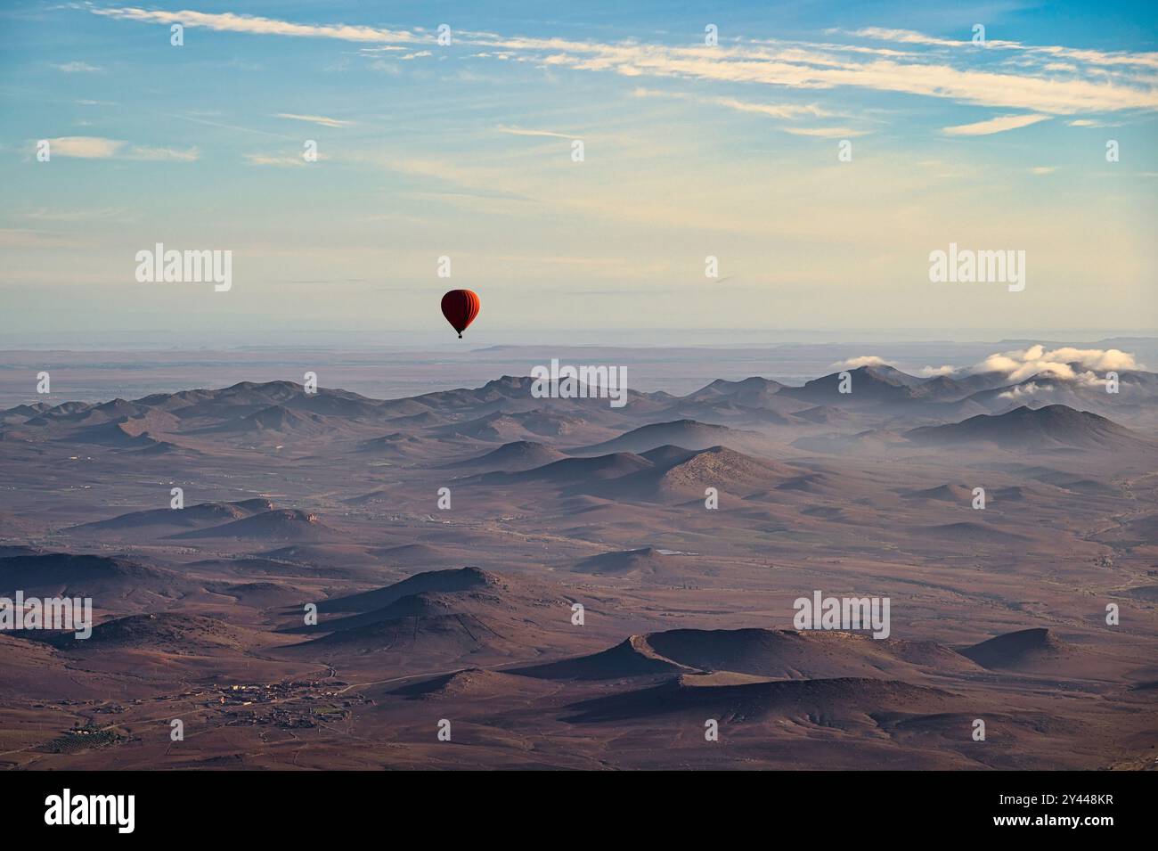 Una mongolfiera rossa, che galleggia sul deserto vicino a Marrakech, in Marocco, in una limpida giornata primaverile, con le montagne innevate dell'Atlante sullo sfondo Foto Stock