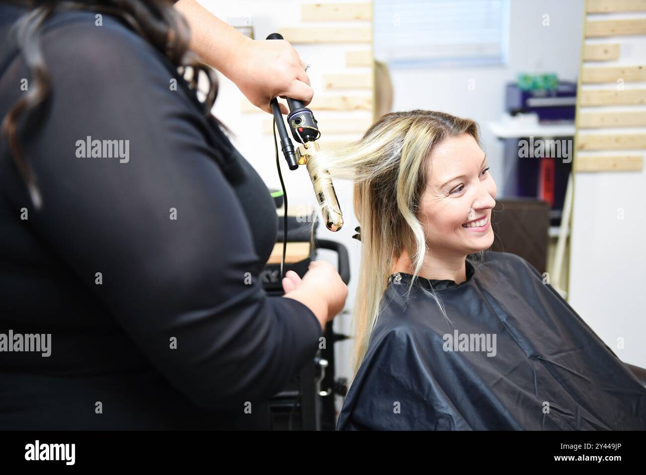 Arricciacapelli clientâ capelli di un parrucchiere con un ferro arricciacapelli, entrambi Foto Stock