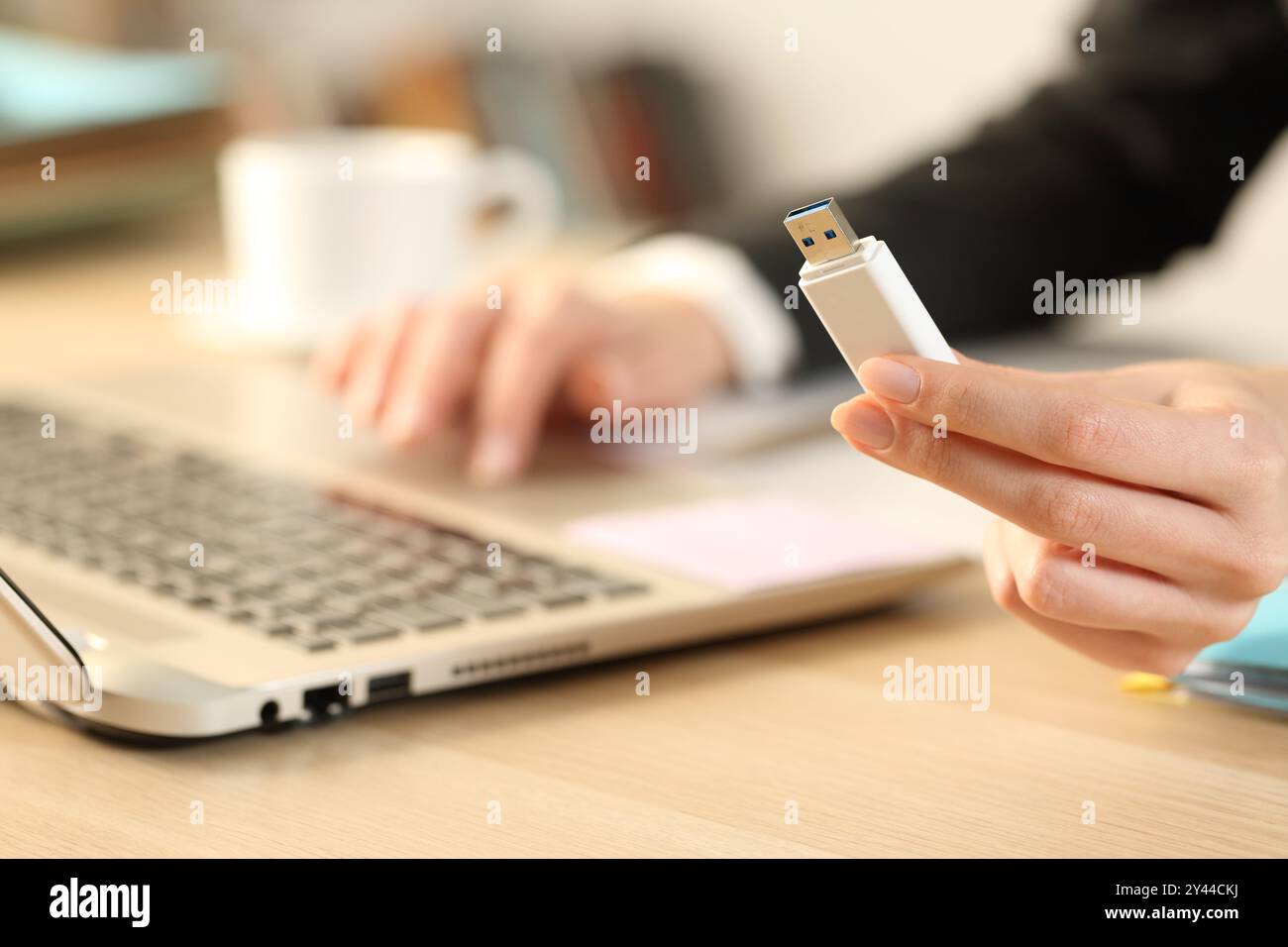Primo piano di un dirigente che tiene in mano un'unità usb utilizzando un computer portatile su una scrivania in ufficio Foto Stock