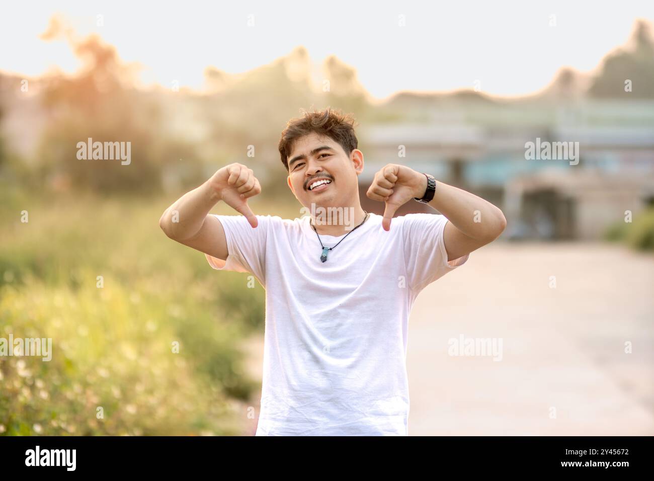 un uomo in piedi con i pollici abbassati. L'uomo si comportava come se qualcuno stesse sottovalutando qualcosa. immerso nella natura in un pomeriggio di sole. Foto Stock