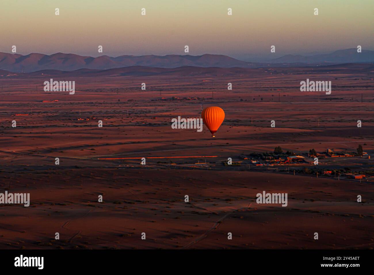 Sorvolando il deserto marocchino, il vibrante palloncino arancione danzerà con la luce dell'alba, dipingendo il cielo con calore e meraviglia Foto Stock