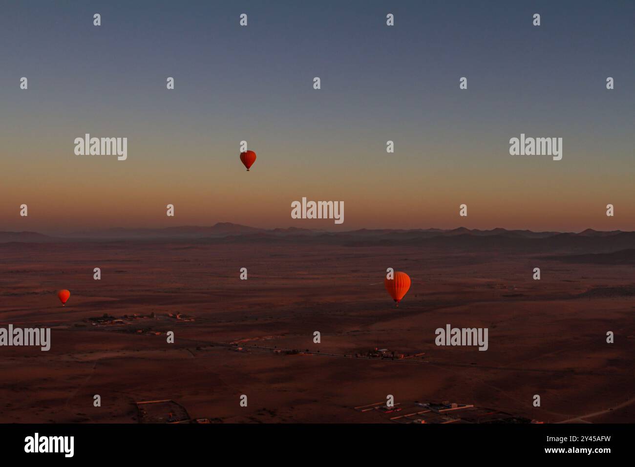 Tre vivaci palloncini arancioni scivolano graziosamente sul vasto deserto marocchino. Foto Stock