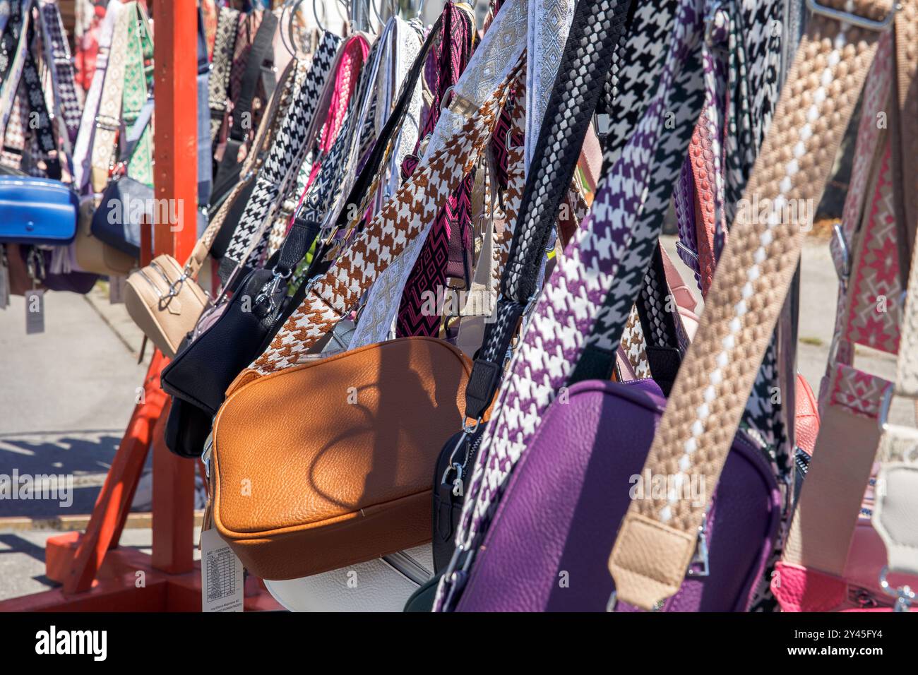 Borse colorate con cinturini a motivi geometrici in una bancarella di mercato alla luce del sole, con accessori vivaci ed eleganti Foto Stock