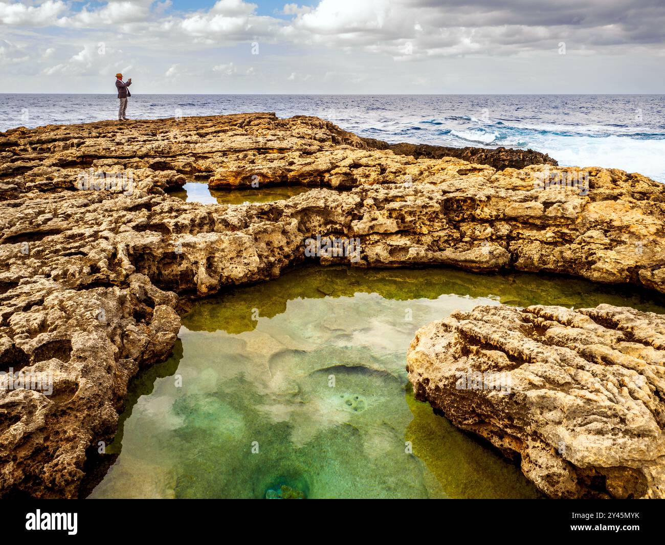 Uomo di scattare una foto in piedi sul calcare corallian marciapiede vicino alla finestra Azzurra - Isola di Gozo, Malta Foto Stock