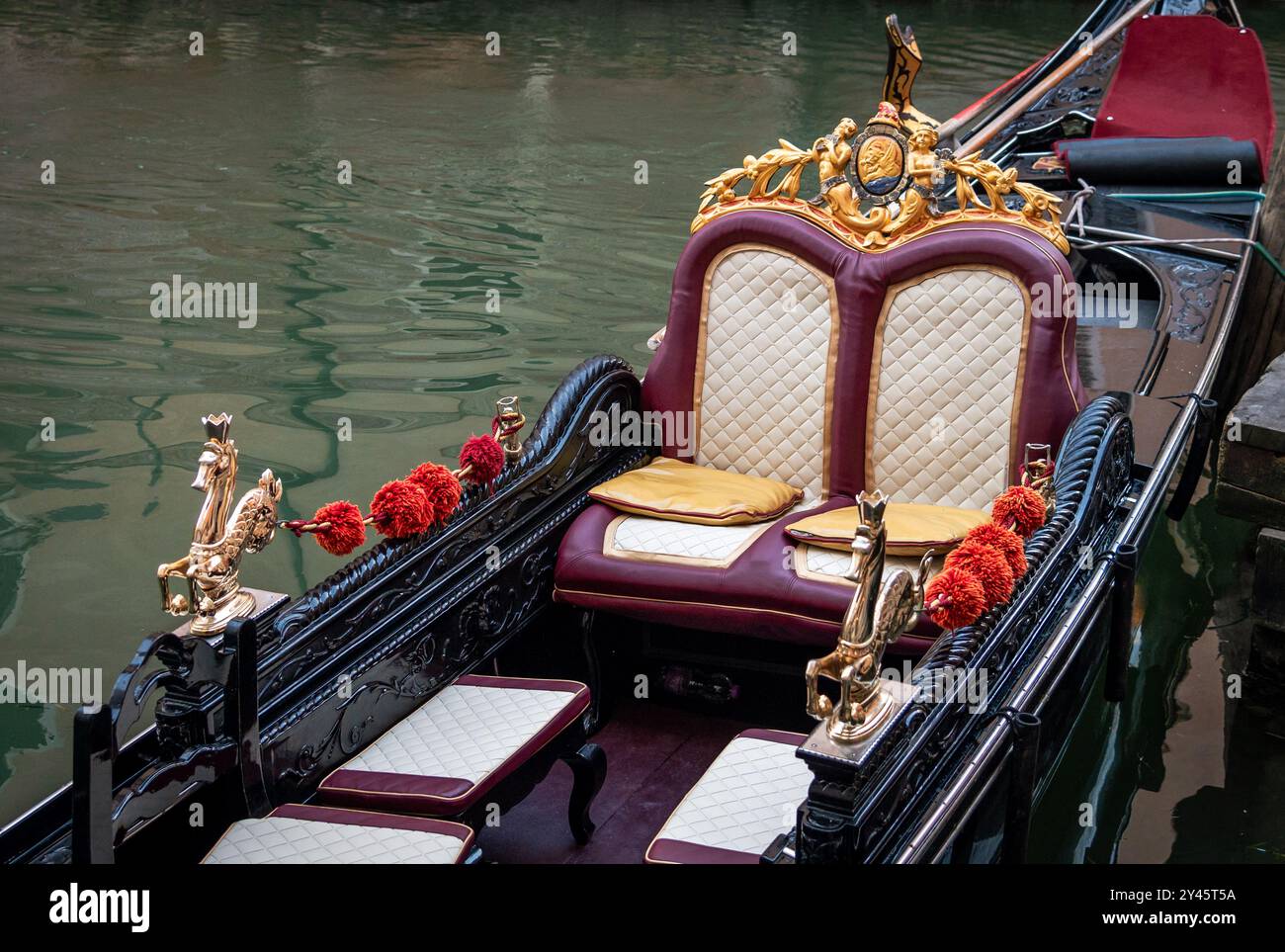Elegante design della gondola con sedili in pelle e decorazioni dorate e ghirlande floreali ormeggiate al molo del canale nella città d'Italia di Venezia Foto Stock