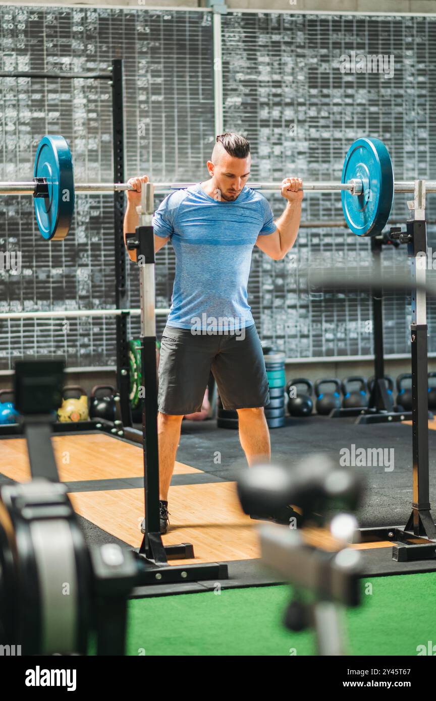 Atleta che solleva pesi in palestra, mostrando forza e potenza durante un esercizio di squat alla schiena. L'ambiente interno con barcampanelli aggiunge intensità a t Foto Stock Atleta che solleva pesi in palestra, mostrando forza e potenza durante un esercizio di squat alla schiena. L'ambiente interno con barcampanelli aggiunge intensità a t Foto Stock