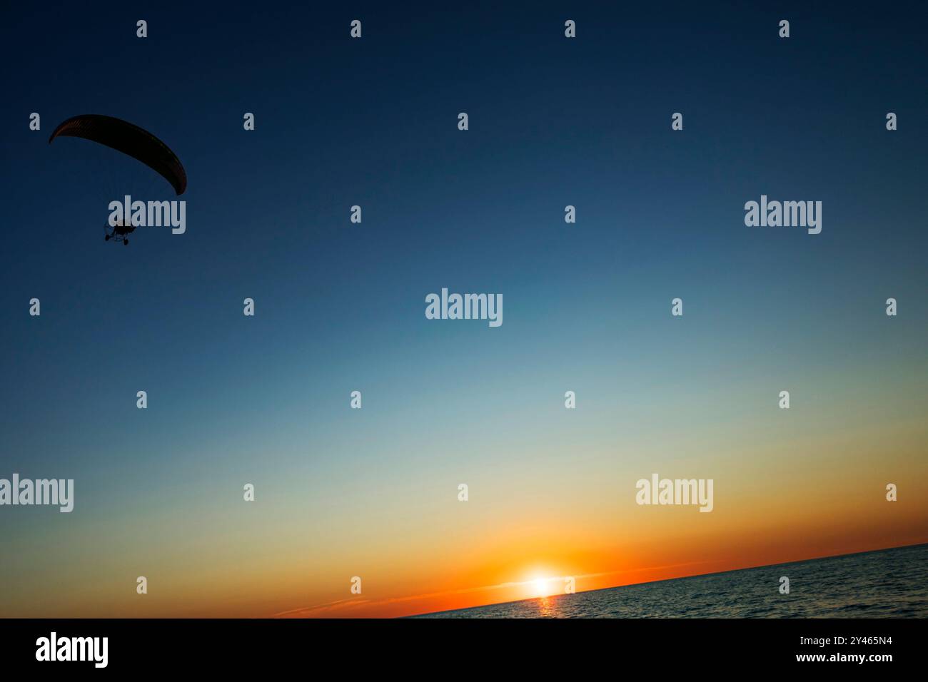 Una persona si sta godendo l'esperienza emozionante di paracadutismo ascensionale sopra lo scintillante oceano sotto i colori vibranti di un bellissimo tramonto Foto Stock