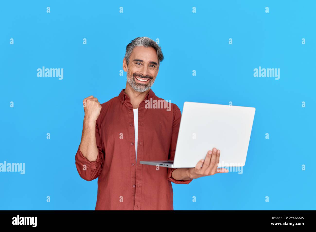 Uomo maturo felice con notebook che celebra la vittoria online isolato su sfondo blu. Foto Stock
