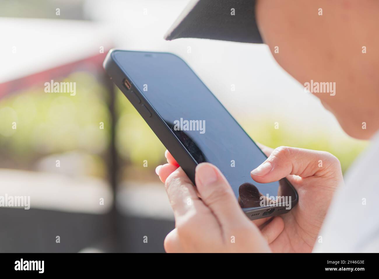 Primo piano di una persona che tiene in mano uno smartphone, concentrandosi sullo schermo. Lo sfondo e' sfocato, suggerendo un ambiente esterno con vegetazione. I pers Foto Stock