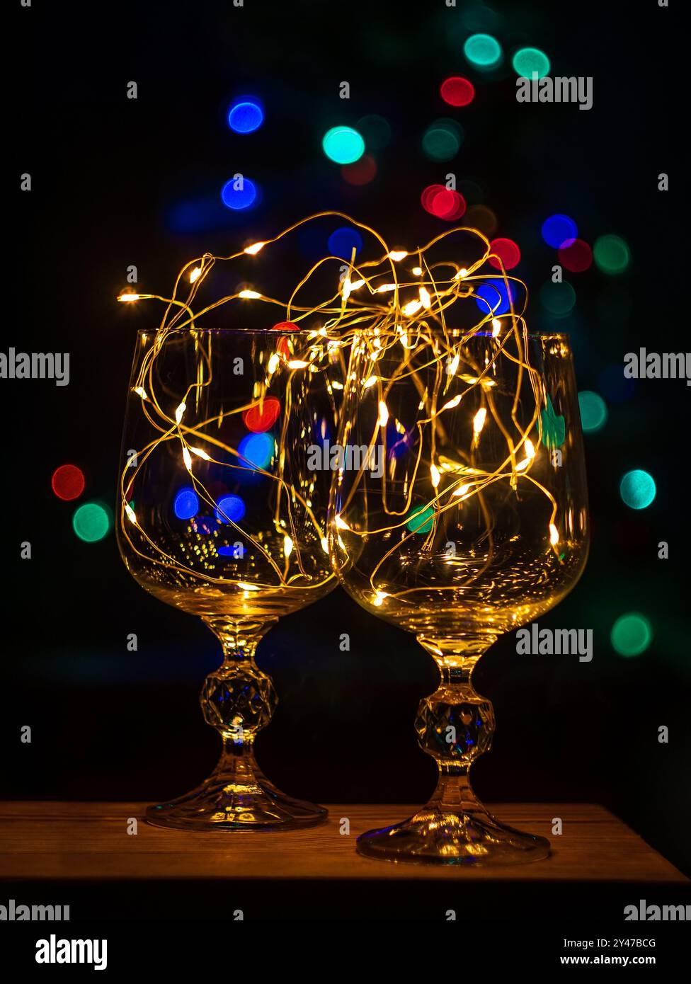 Bicchieri da vino di cristallo con ghirlanda dorata su tavola di Natale bokeh luce sfondo verticale salvaschermo. Cena romantica di Capodanno con champagne Foto Stock