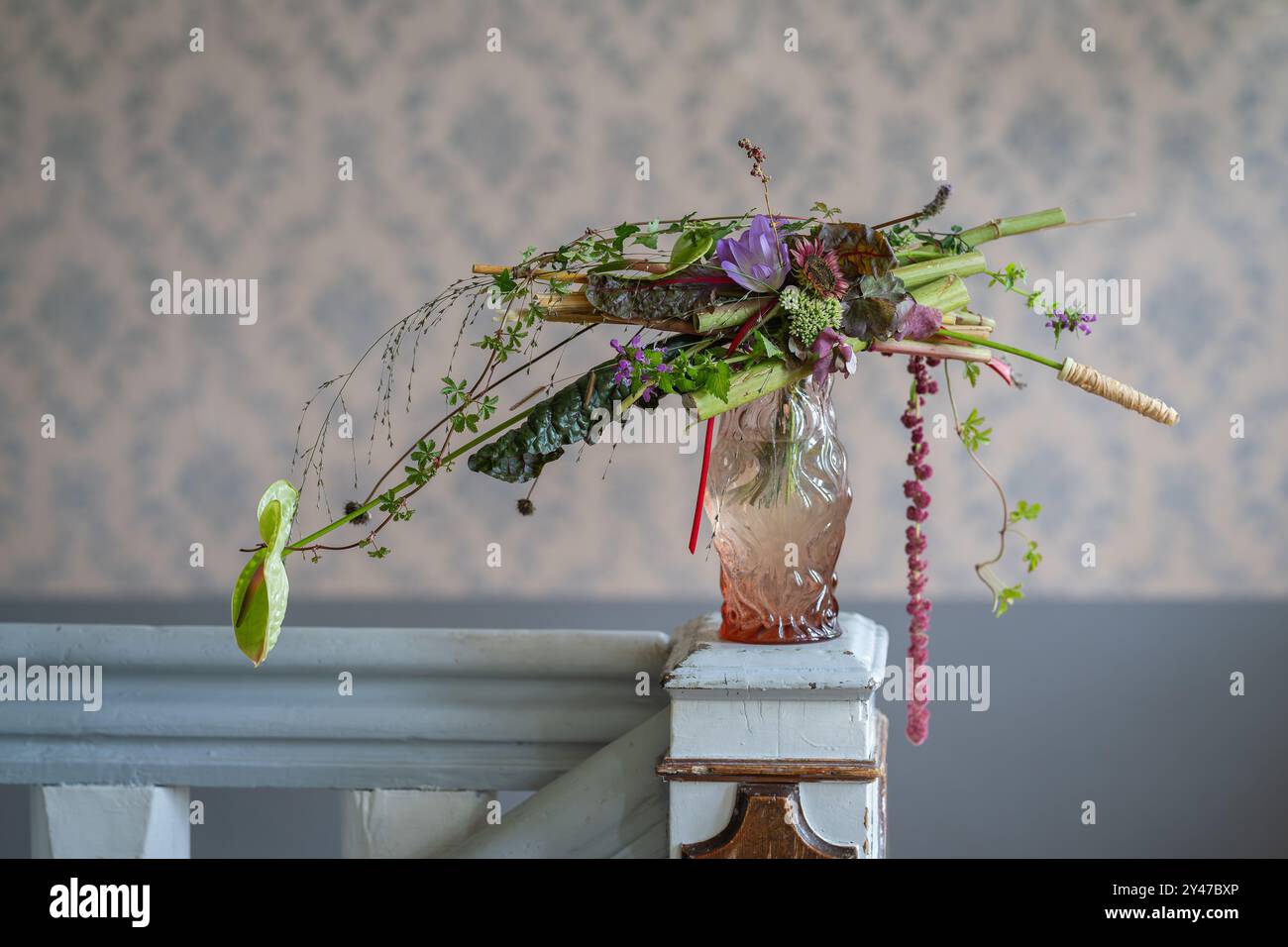 Composizione floreale autunnale di cavolo, fiori autunnali e rami. Design degli interni con bouquet in vaso di vetro su colonna in legno. Foto Stock