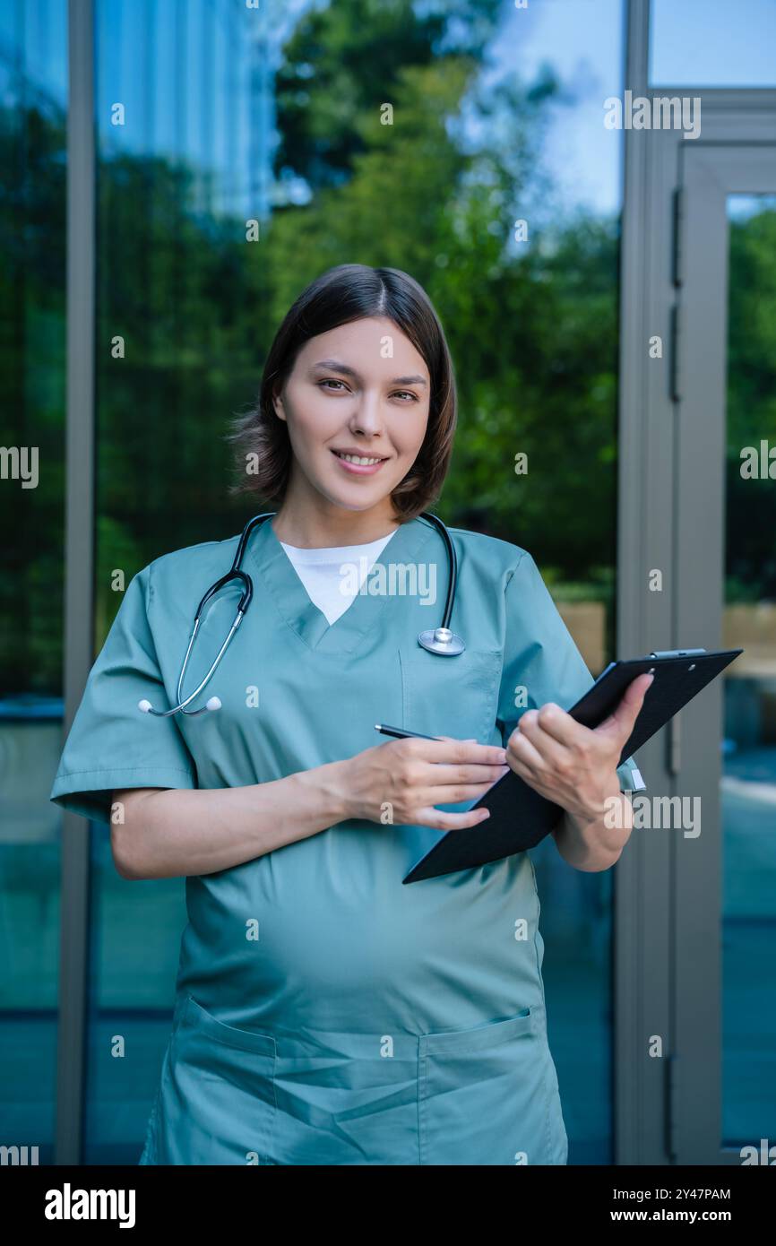 Gravidanza sorridente giovane medico con un elenco di prescrizioni in mano Foto Stock