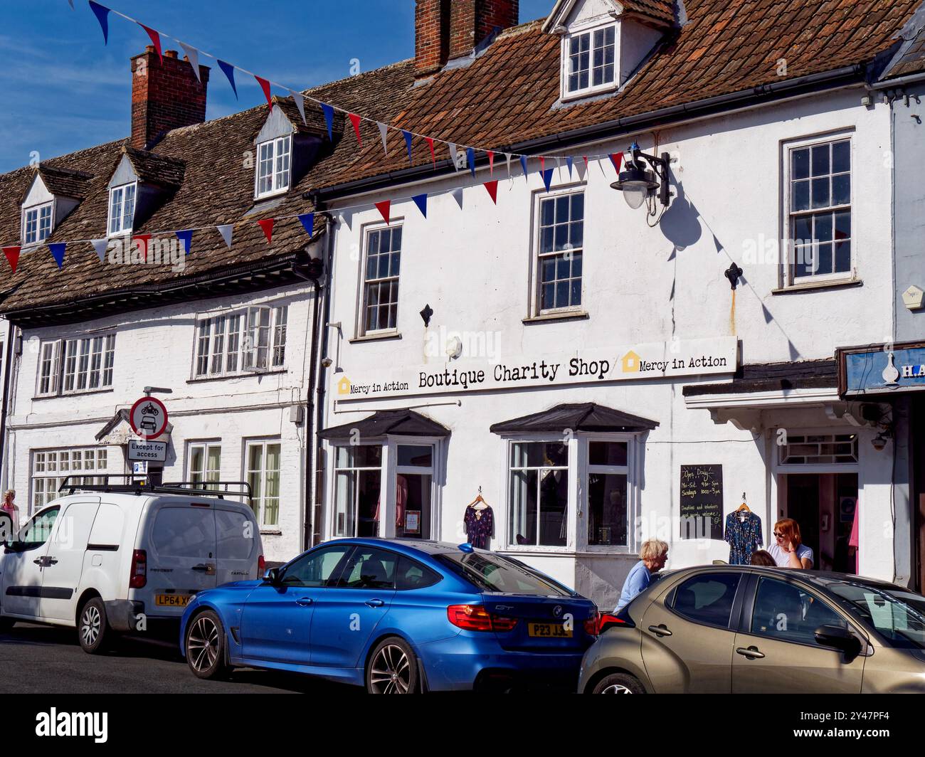 Bunting è collegato al Mercy in Action Boutique Charity Shop con volontari all'esterno e parcheggiate auto a Highworth, Wiltshire, Inghilterra Foto Stock