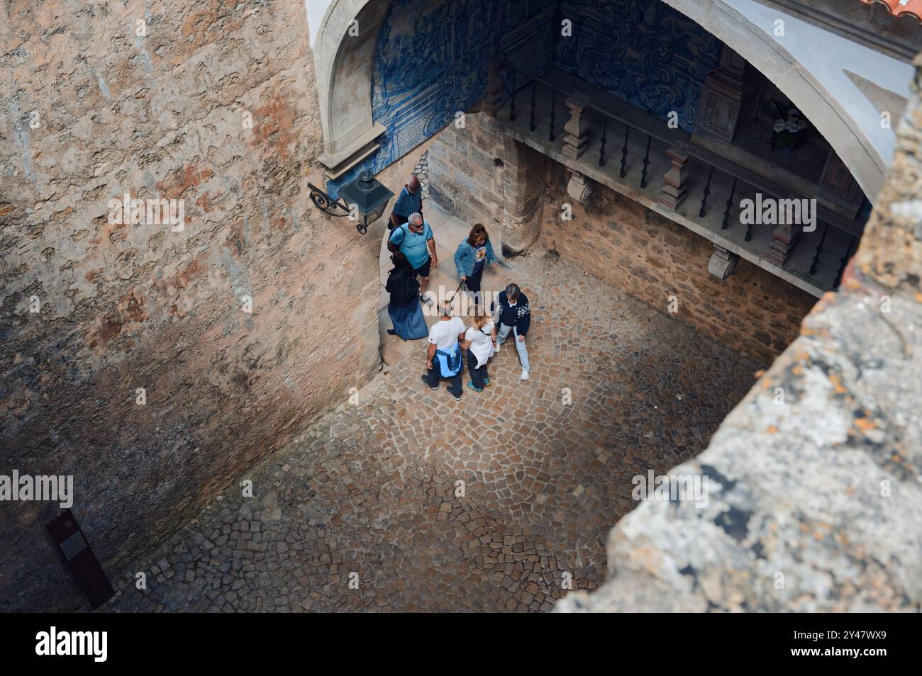 Un gruppo di turisti passa sotto un arco di ciottoli nelle strade storiche di Óbidos Foto Stock