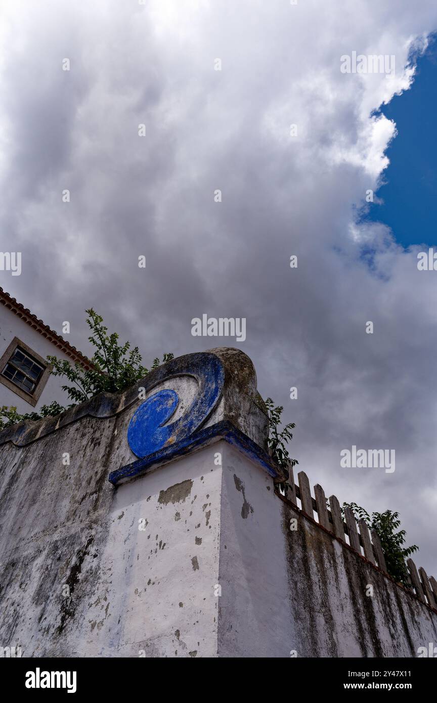 Le pareti intemprate con un dettaglio blu a turbolenza si stagliano contro un cielo dolente a Óbidos Foto Stock