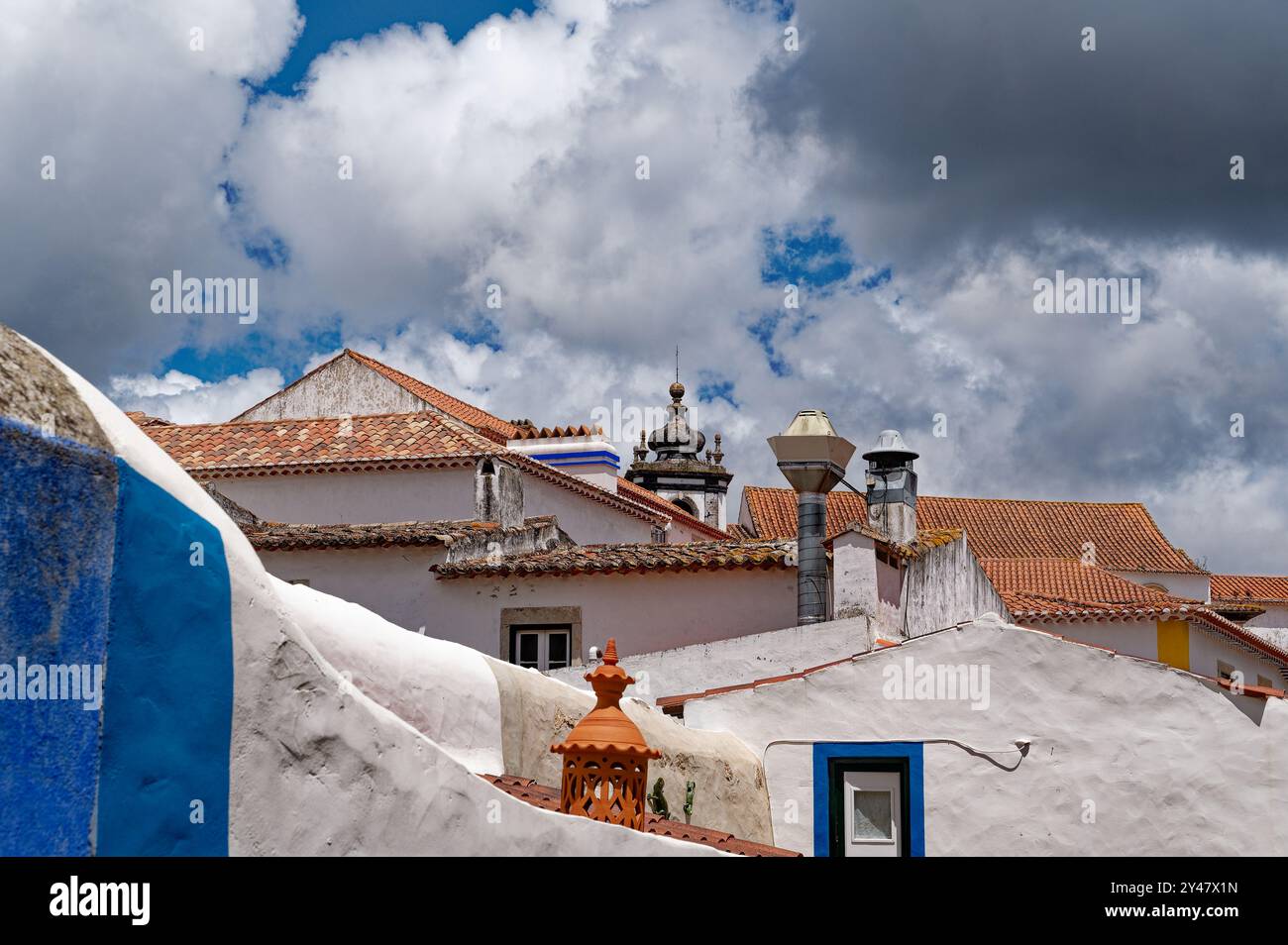 Tetti di tradizionali piastrelle di terracotta e dettagli ornati sotto le nuvole drammatiche a Óbidos Foto Stock