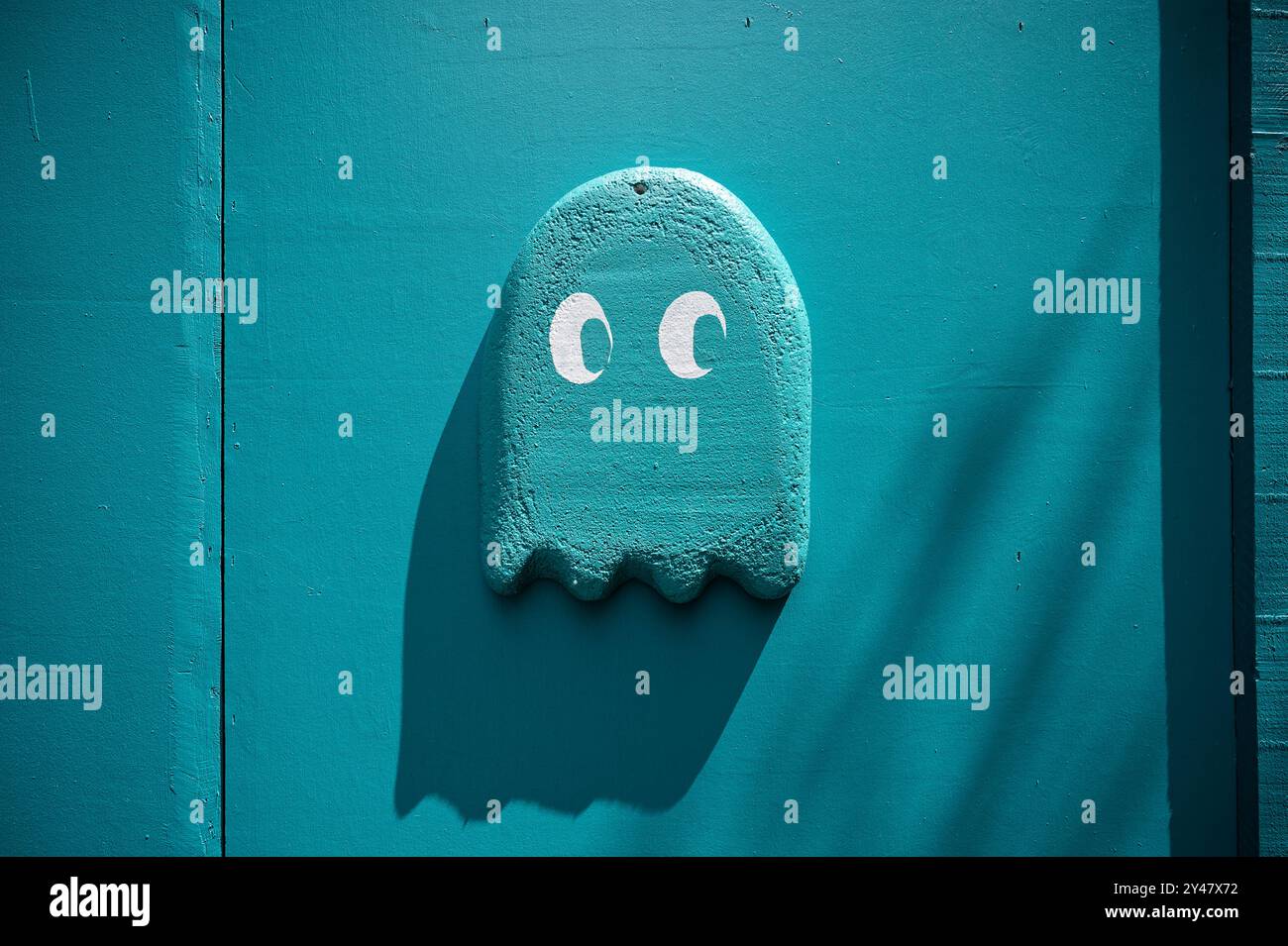 Una rappresentazione giocosa di un fantasma 'PAC-Man' è dipinta in vivaci tonalità blu su una parete testurizzata, che si fonde con l'ambiente circostante Foto Stock