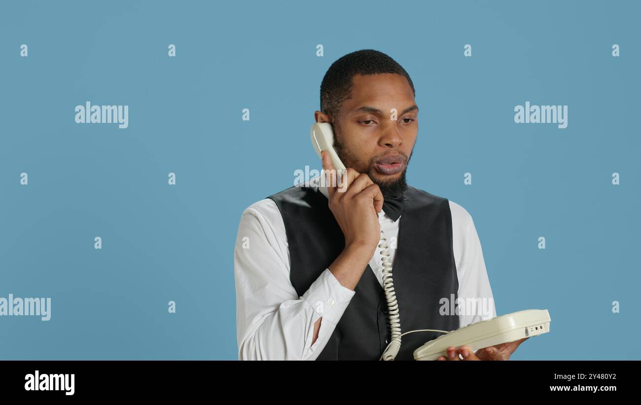 Il personale di portineria risponde al telefono fisso per prenotare, discutendo con i clienti delle camere e dei servizi di un hotel a cinque stelle. Utilizzo del telefono con cavo come ausilio. Telecamera A.. Foto Stock
