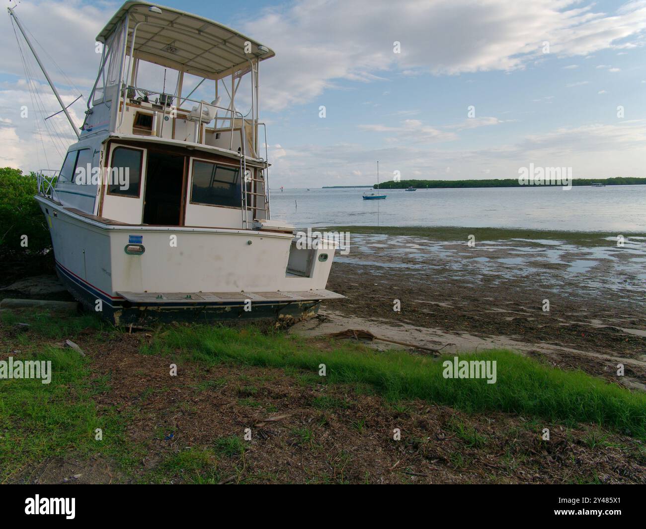 Ampia vista sulle pozzanghere con bassa marea verso il grande peschereccio bianco abbandonato sulla riva dell'acqua del Maximo Park verso il canale Skyway Foto Stock