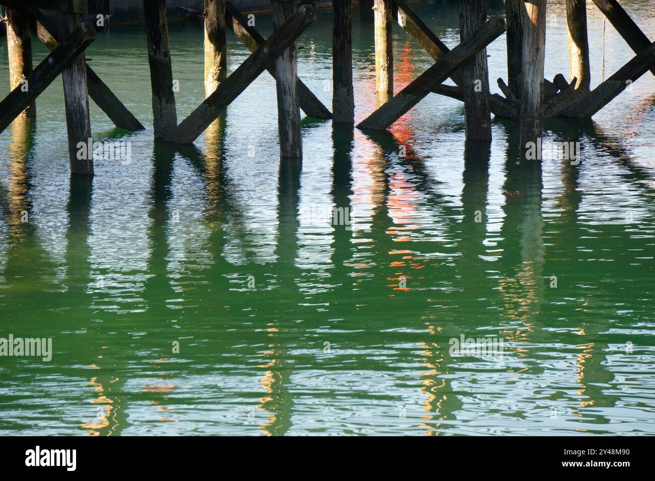 Vista di piloni in legno e riflessi scintillanti sotto un molo Foto Stock