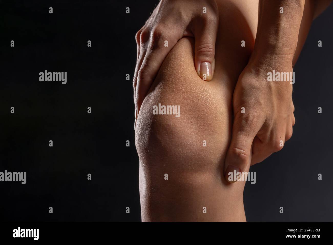 donna mani primo piano che preme sull'articolazione del ginocchio su sfondo scuro, concetto di dolore al ginocchio, trattamento del dolore alle gambe Foto Stock