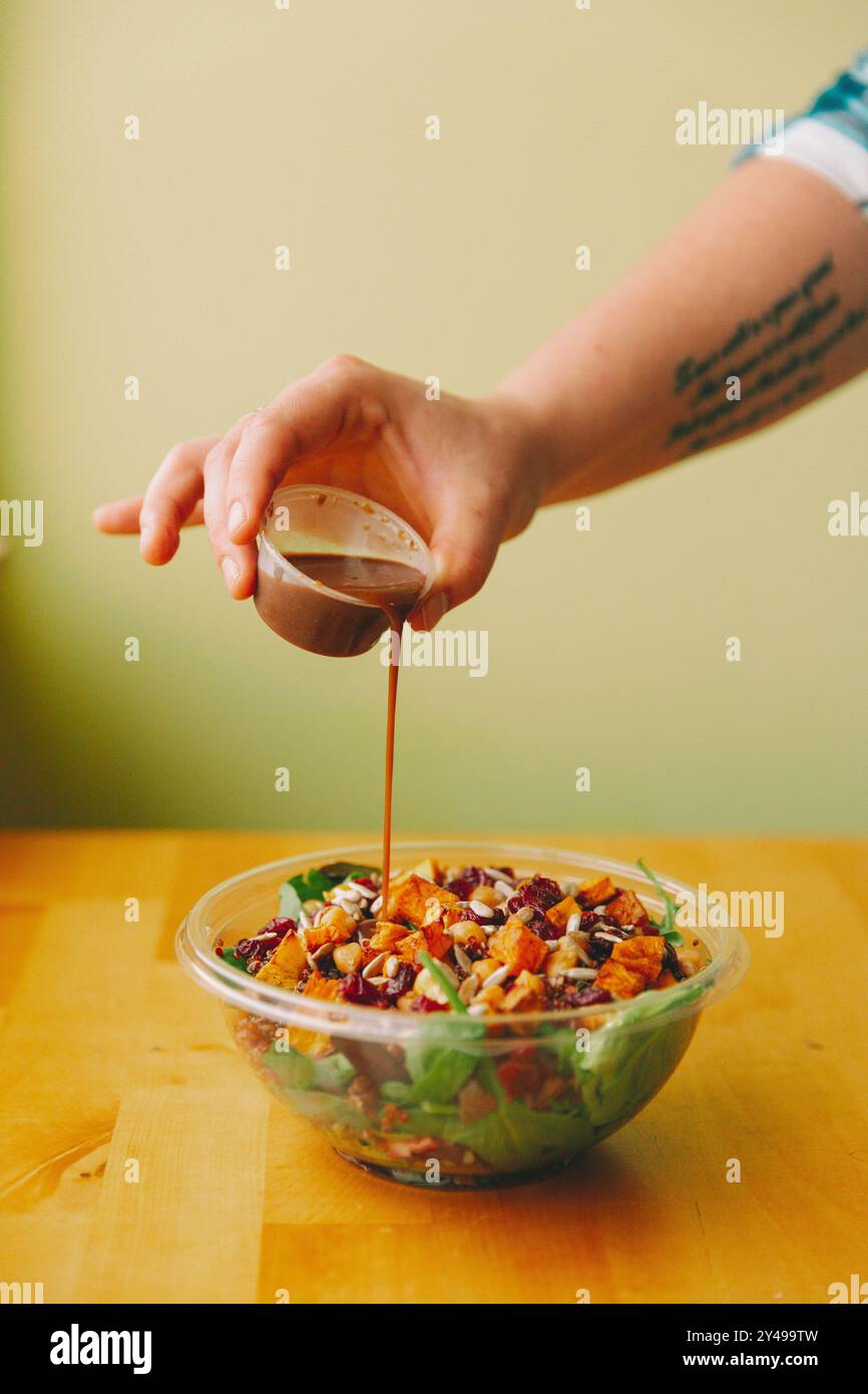 Una mano che versa il condimento su un'insalata. Foto Stock